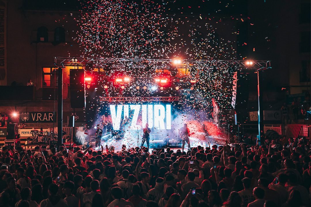 Concert a la plaça de nit amb confeti sobre l'escenari i el públic
