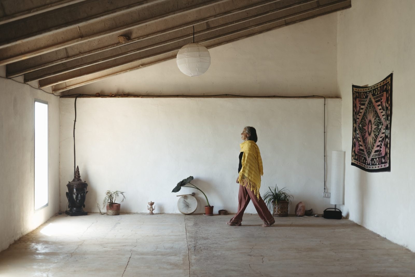 Una dona caminant descalça per una sala blanca amb bigues de fusta
