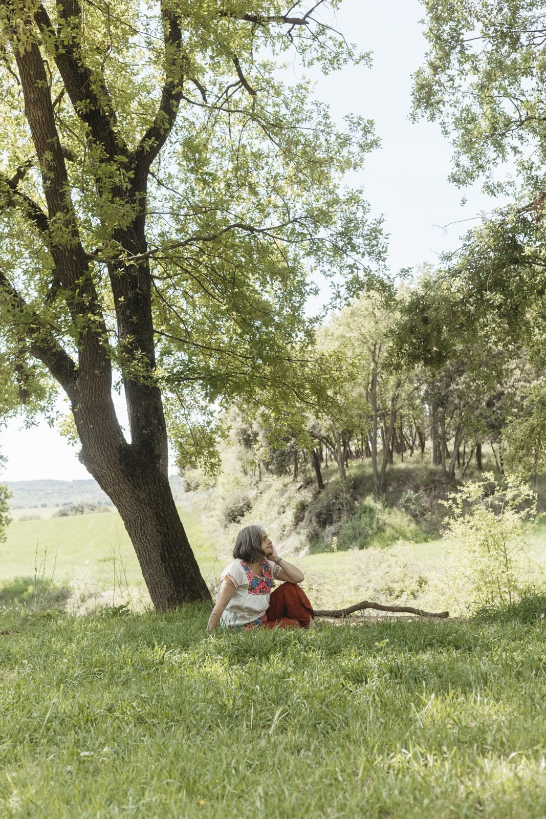 Una dona asseguda a l'herba sota un arbre