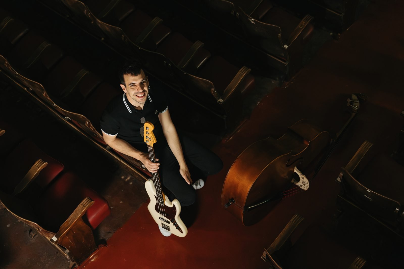 Músic assegut entre les butaques d'un teatre amb el baix elèctric i el contrabaix