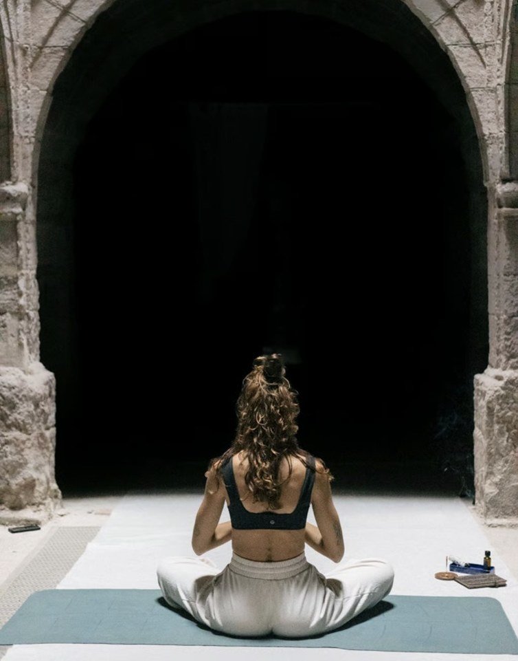 Professora de ioga meditant d'esquena davant un arc de pedra