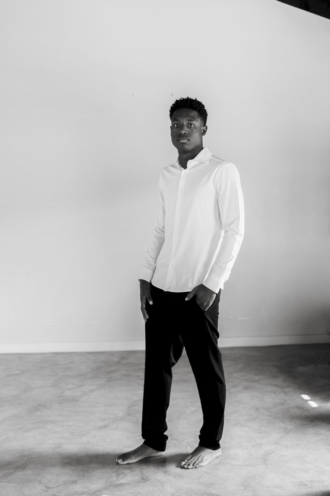 Retrat editorial en blanc i negre d'un noi amb camisa blanca, descalç